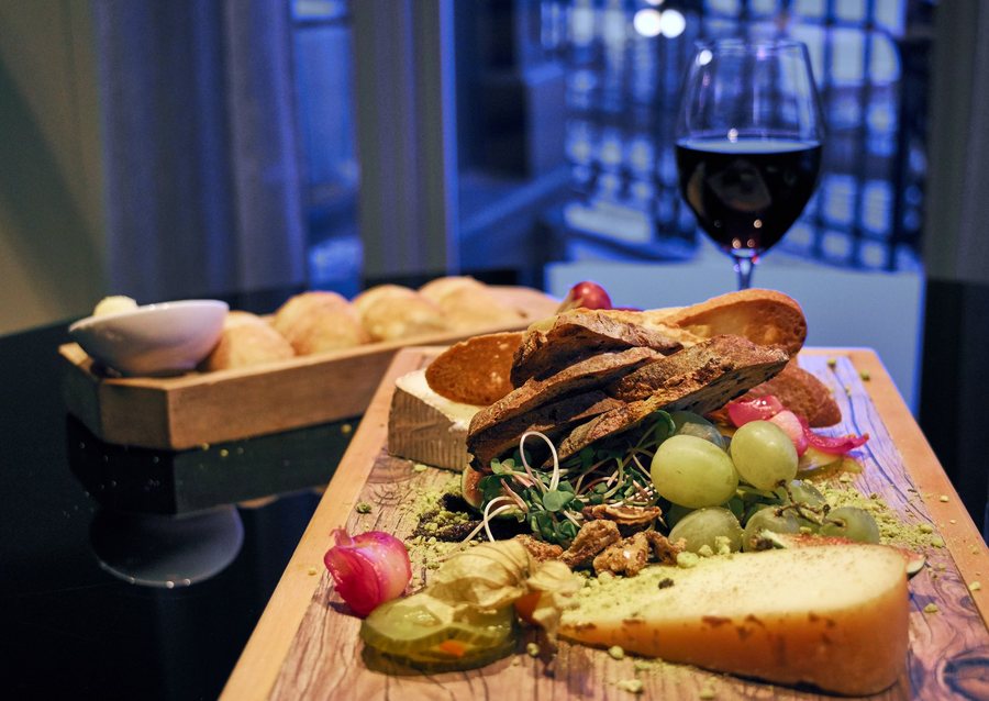 Un plateau de bois avec du fromage, du raisin, du pain grillé et un verre de vin rouge