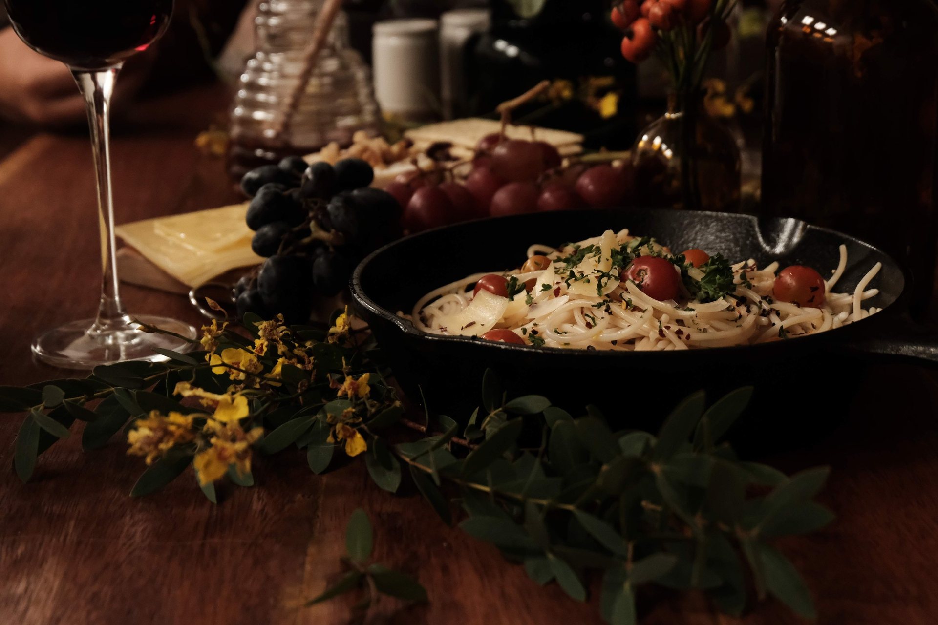 Une poêle de pâtes aux tomates cerises, du raisin, du fromage et un verre de vin sur une table de bois, le soir
