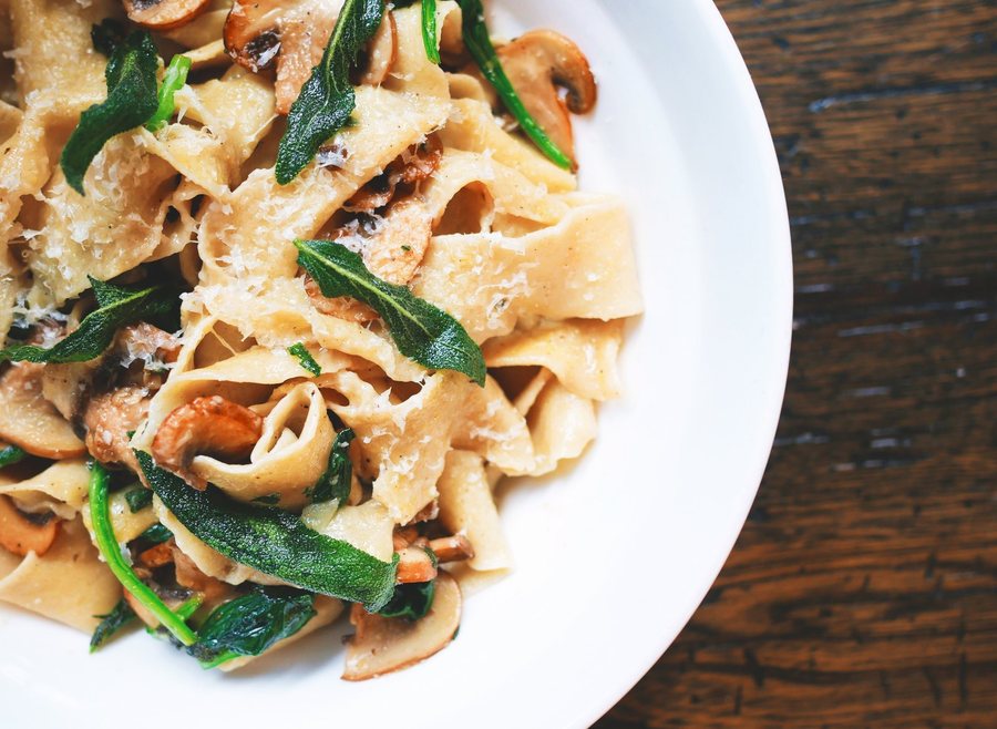 Des pappardelle aux champignons et aux feuilles vertes, parsemées de parmesan